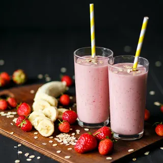 Two smoothie with a banana and strawberries surrounding them